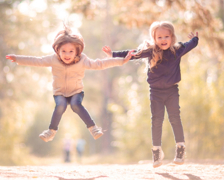 Two little girls jumping and playing together outdoors